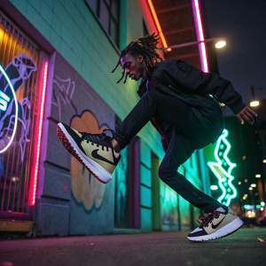 Playboi Carti's Nike sneaker, against a backdrop of neon colors and graffiti. A young person with dreadlocks, jumping in the air.