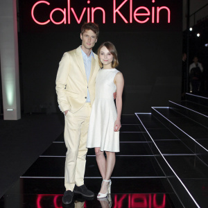 Emily Browning and Max Irons at the Calvin Klein Fashion Show. On a sleek, black stage with neon Calvin Klein logos.