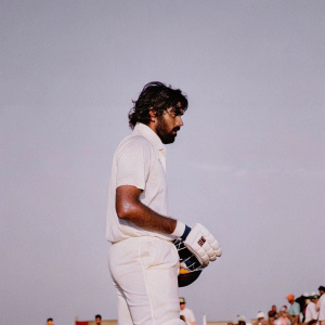 Nuwan Pradeep, Sri Lankan cricketer, intense gaze. Bearded face. Wearing cricket uniform. Pitch ambiance. Spectators visible.