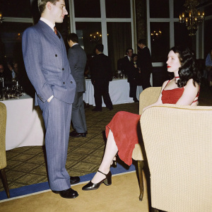 Yuri Milner and Julia Milner at the annual tech gala. Yuri in a sharp suit, Julia in an elegant red dress. Crowded room, guests mingling