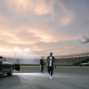 Achraf Hakimi, wearing a black and white jersey, walking confidently towards a stadium. A luxury car and a VIP host stand beside him.