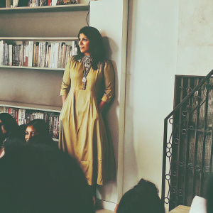 Konkona Sen Sharma at the Book Launch. Wearing a mustard dress with a structured neckline and a prominent necklace. Standing against a white backdrop. The event is filled with books and promotional material.
