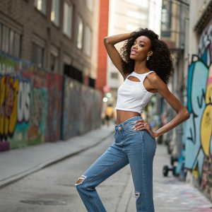 Winnie Harlow on the set of a magazine photoshoot. Wearing a simple white top and jeans. Urban street background with graffiti.