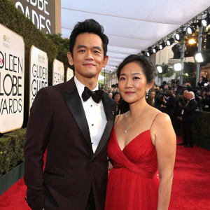 John Cho and Kerri Higuchi at the Golden Globe Awards. John in black tuxedo. Kerri in elegant red gown. Red carpet setting