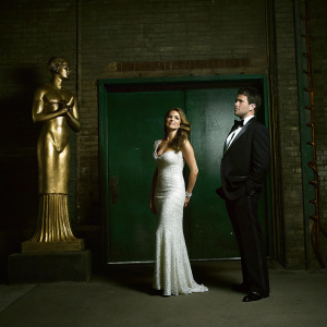 Sofia Vergara and Manolo Vergara on the Met Gala red carpet. Sofia wears a stunning white sequined gown. Manolo is in a black tuxedo. Behind them, a large golden statue stands out