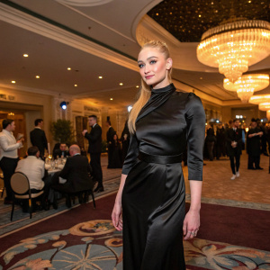 Sophie Turner in a black silk dress, attending the launch event for Game of Thrones season finale. The venue is a posh hotel ballroom, guests milling around.