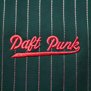 Close-up of Daft Punk's logo. Textured red cursive font on a dark green striped background. Sewn fabric technique.