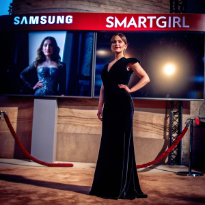 Blanca Suarez stands confidently in a sleek black velvet gown. Samsung and SMARTgirl logos prominently displayed. Simple white background. Immaculate portrait photo