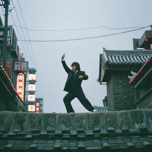 Jackie Chan in a dynamic martial arts pose. Dark suit, urban setting with neon lights. Photo