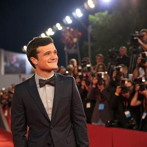 Josh Hutcherson at an awards show. Wearing a dark suit and bow tie. The backdrop is a sea of flashing cameras and excited fans.