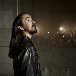 Steve Aoki, DJ and music producer, in a dynamic digital illustration. He sports a beard and long dark hair, wearing a black leather shirt, against a vibrant orange backdrop filled with pulsating lights and enthusiastic crowd.