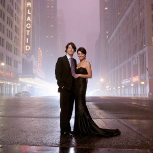 Sandra Bullock and Keanu Reeves, dressed in formal attire, posing for a glamorous photo shoot on a bustling city street at night.
