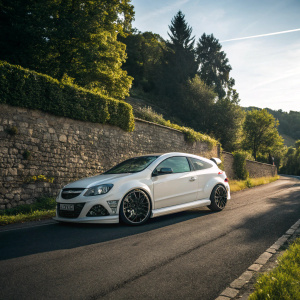 Photograph of the sporty Opel Astra H OPC Nurburgring Edition parked on an asphalt road. Stone wall and greenery backdrop. Sun casting shadows, natural light.