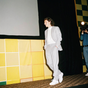 Tom Holland, standing casually at Spider-Man event in South Korea. Brightly lit stage with multicolored backdrop