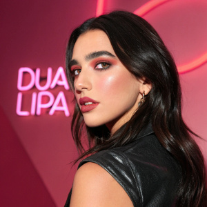 Dua Lipa in a striking photo shoot. Bold, pink logo 'Dua Lipa' in the background. Shiny, multi-angled shot emphasizing her long, dark hair and makeup.