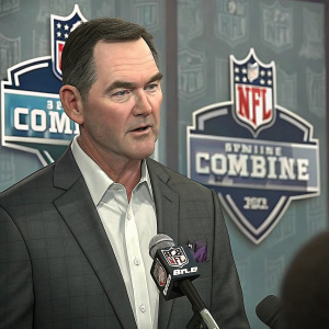 Mike Zimmer, wearing a dark gray suit, addressing reporters at a press conference. Large NFL Combine banners and logos behind him.