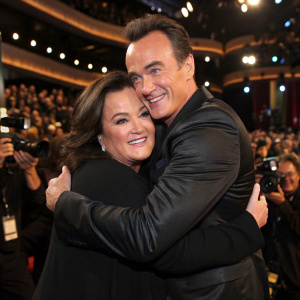 Rosie O'Donnell and Julian McMahon hugging at an award show. Studio audience and photographers in the background.