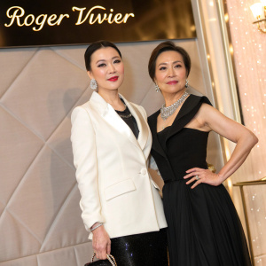 Carina Lau and Cherie Chung posing for a glamorous photo shoot. Luxurious backdrop featuring Roger Vivier logo. Carina in a chic white blazer and black gown. Cherie in a sleek black top.