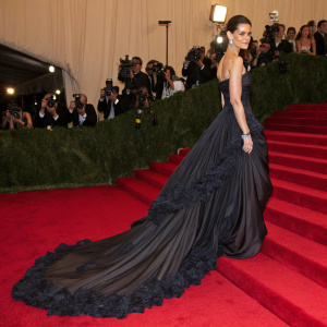 Katie Holmes, in a flowing black evening gown with dramatic train and intricate ruffles, graces the red carpet of a high-profile awards ceremony.