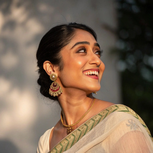 Regina Cassandra, Indian actress, radiant smile. Wearing traditional attire, shot against a blurred, shadowy background.