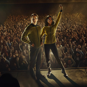 High-resolution image: Chris Pine and Zoe Saldana on stage at a Star Trek convention. They wear costumes from the latest series. Audience cheering in the background.