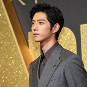 Jing Boran, Chinese actor, at award ceremony. Grey suit, black hair, serious look, against gold textured backdrop