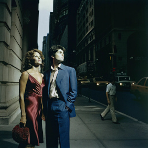 Riccardo Scamarcio and Valeria Golino on a bustling New York City street, Riccardo in a blue suit, Valeria in a shimmering red dress.