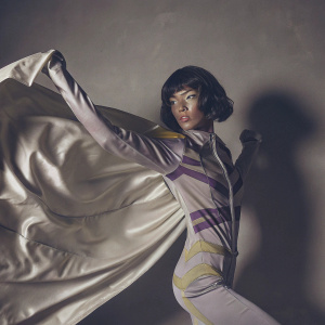 Kim Jung Gi, a dynamic female character, wears a futuristic outfit in shades of gray, purple, and yellow. The metallic-like costume gleams against a plain, neutral gray backdrop. Rendered in vivid 3D, she strikes a powerful pose.