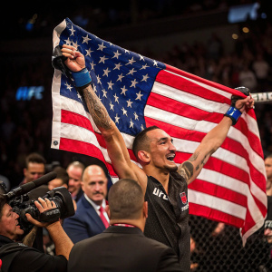 Max Holloway, UFC champion, waving a large US flag after winning. Surrounded by cheering fans and UFC officials.