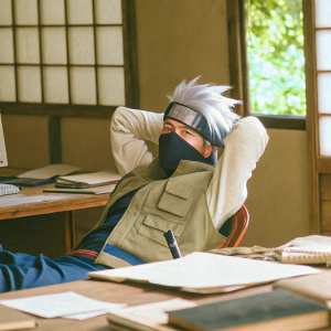 Realistic pencil drawing of Kakashi from Naruto. Sitting in an office setting with a messy desk, computer, and books scattered around.