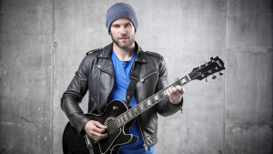 A 30-year-old man in a black leather jacket and a gray beanie hat sits on a chair with a black guitar, stock photo James Baines, winner of the Shutterstock competition, neoplasticism, stock photo, stock photo, studio photo
