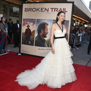 Olivia Cheng, celebrating the release of 'Broken Trail' at the premiere. Wearing a stunning white gown with a crinoline skirt and black belt. Surrounded by movie posters and fans on the red carpet.