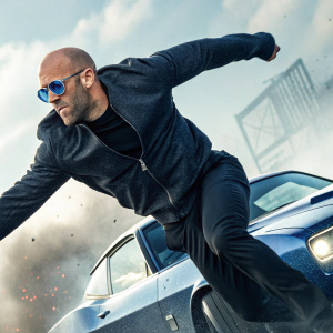 Jason Statham on the cover of 'Transporter 2'. Statham, wearing blue sunglasses, mid-jump, mid-action scene. Fast car in background, blurred motion