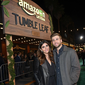 Jamie-Lynn Sigler and her son Beau Kyle Dykstra, attending the premiere of Amazon Original Series Tumble Leaf. They stand in front of a large wooden sign featuring Amazon branding. The event is held in a bustling theater in Los Angeles.