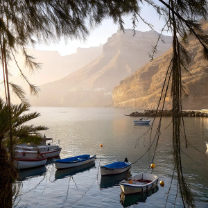 Stunning photo of Puerto de Mogan, Gran Canaria. Small boats anchored in the serene harbor. Majestic mountains in the backdrop. Crystal blue sea