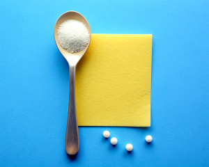 big spoon of sugar, near a yellow sticky note and medicine. top view. Blue background. 