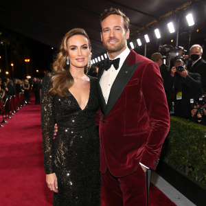 Elizabeth Chambers and Armie Hammer at the Oscars afterparty. Elizabeth in a black sequined gown, Armie in a maroon velvet suit. Flashy red carpet with paparazzi in the background.