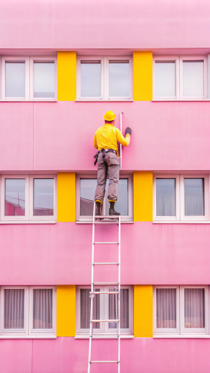 four floors gray building worker washes window on second floor stands on stepladder