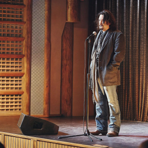 Johnny Depp, with a rugged appearance, sporting a goatee and shaggy dark hair. Attending the Sundance Film Festival, standing alone on stage.