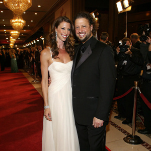Shannon Elizabeth and Joseph D. Reitman at a Hollywood awards gala. Elizabeth, in a flowing white gown, and Reitman, in a sleek black tuxedo, beam as they pose for photographers amidst a sea of celebrities.