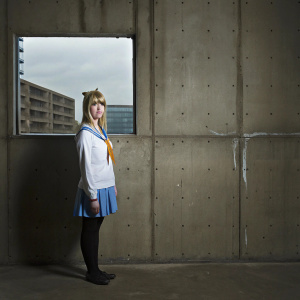 Chitoge Kirisaki from Nisekoi anime series, vibrant look with a mix of Caucasian and anime features, blonde hair, blue eyes. White shirt with blue collar, blue skirt, orange accessory. Dark cityscape backdrop.