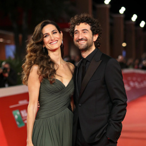 Stefania Spampinato and Alessandro Siani, dressed in formal attire, posing at the film festival gala. Stefania with flowing brunette hair, Alessandro with curly dark hair and a black suit. Both smile warmly against a red carpet backdrop.