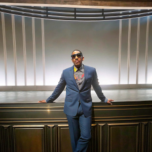 Chris 'Ludacris' Bridges at the Grammy Awards. Dapper in a dark blue suit, colorful shirt, and shades. Formal stage backdrop with lighting