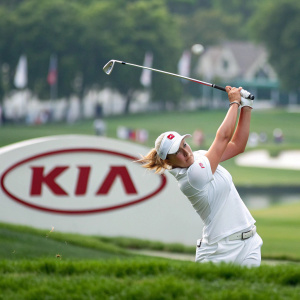 Cristie Kerr in a dynamic golf swing pose at the PGA Championship. White golf shirt and matching hat. Kia logo in the background.