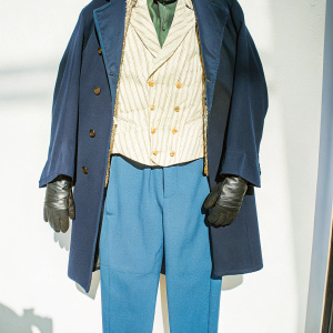 Costume design inspired by Tom Hardy's character from 'Taboo'. Black coat, layered vest, dark trousers, and gloves. White background, photo