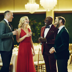 Matt Iseman, Kristine Leahy, Steve Wilkos, and Akbar Gbajabiamila at a gala dinner. They are dressed in formal attire. The dimly lit room with restaurant decor is filled with laughter and lively conversations.