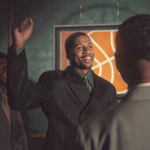 Allen Iverson, dressed in a dark suit, celebrating at the NBA Hall of Fame induction. Large illuminated backdrop with basketball logo.