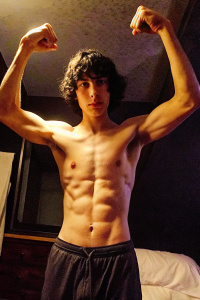 Selfie of Finn Wolfhard flexxing muscles at night, flash on, big chest, sweaty, looking down, view from below, showing armpits, relaxing on bed shirtless, wearing boxers underpants, sweaty, selfie, arms behind his neck
