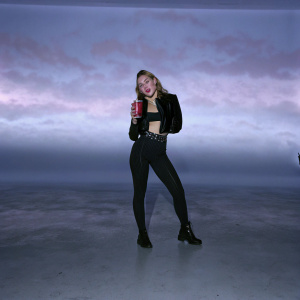 Miley Cyrus, posing with a Coca-Cola can. Studio photo, pink gradient background.