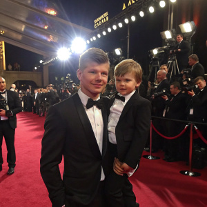Andrey Arshavin and his son Artem posing at a glamorous award ceremony. Flashing lights from numerous cameras
